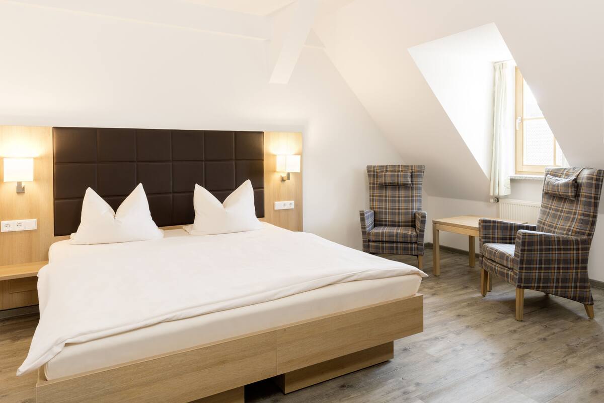 A modern hotel room with a large bed, two armchairs, a small table, and a skylight.