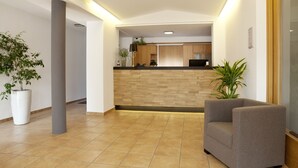 A modern lobby with a reception desk, a grey armchair, and potted plants. - Gasthof Lerner (Freising)
