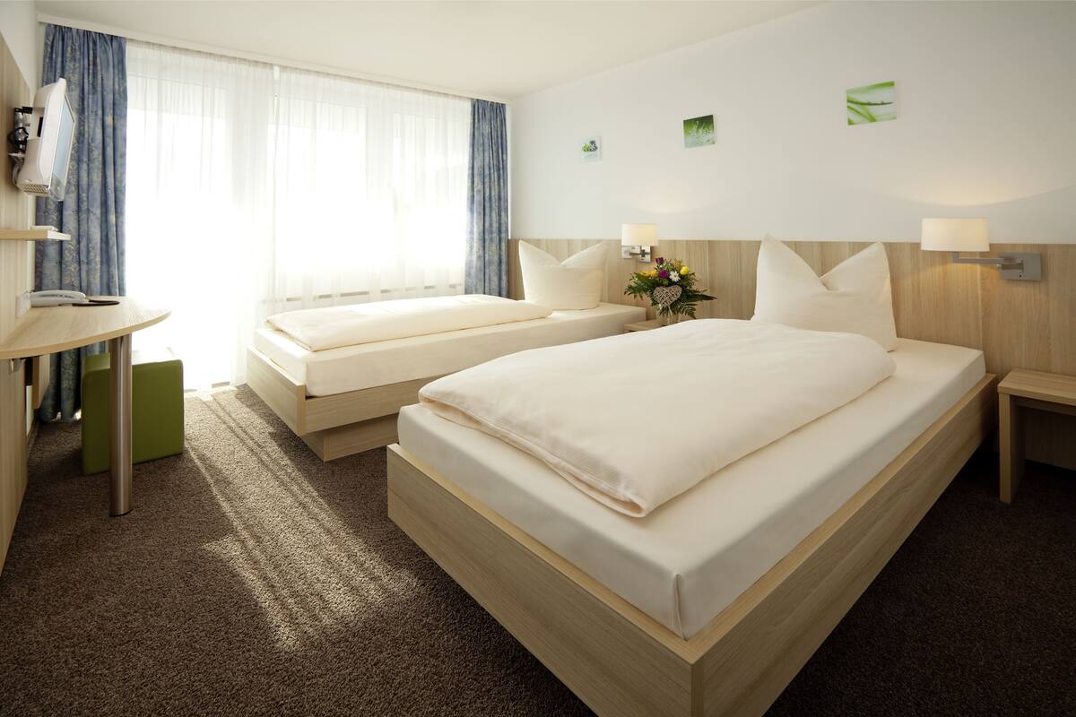 A hotel room with two beds, a desk, and a small green stool.