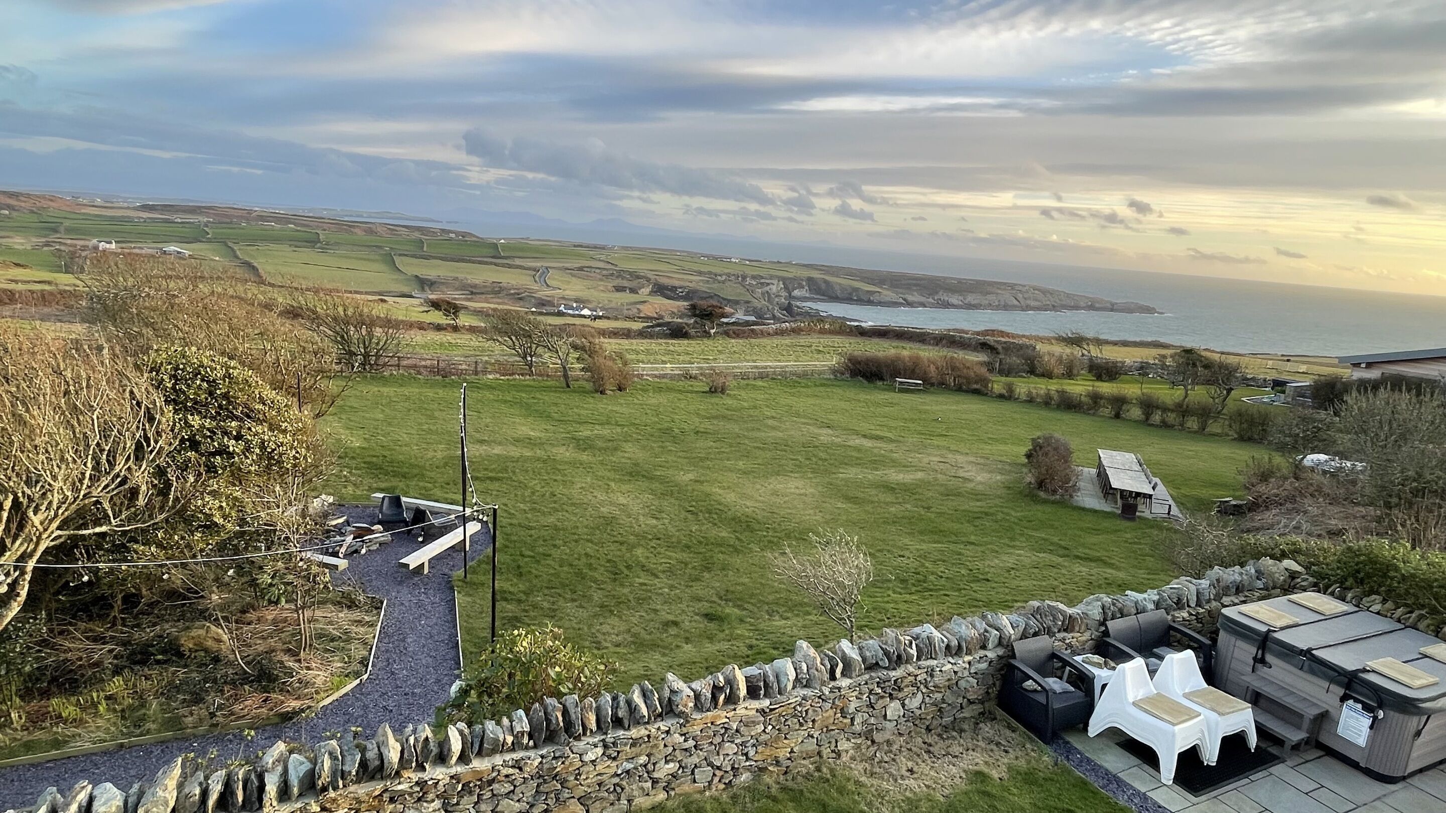 A scenic view of a coastal property with a stone wall, outdoor seating, and a grassy lawn.