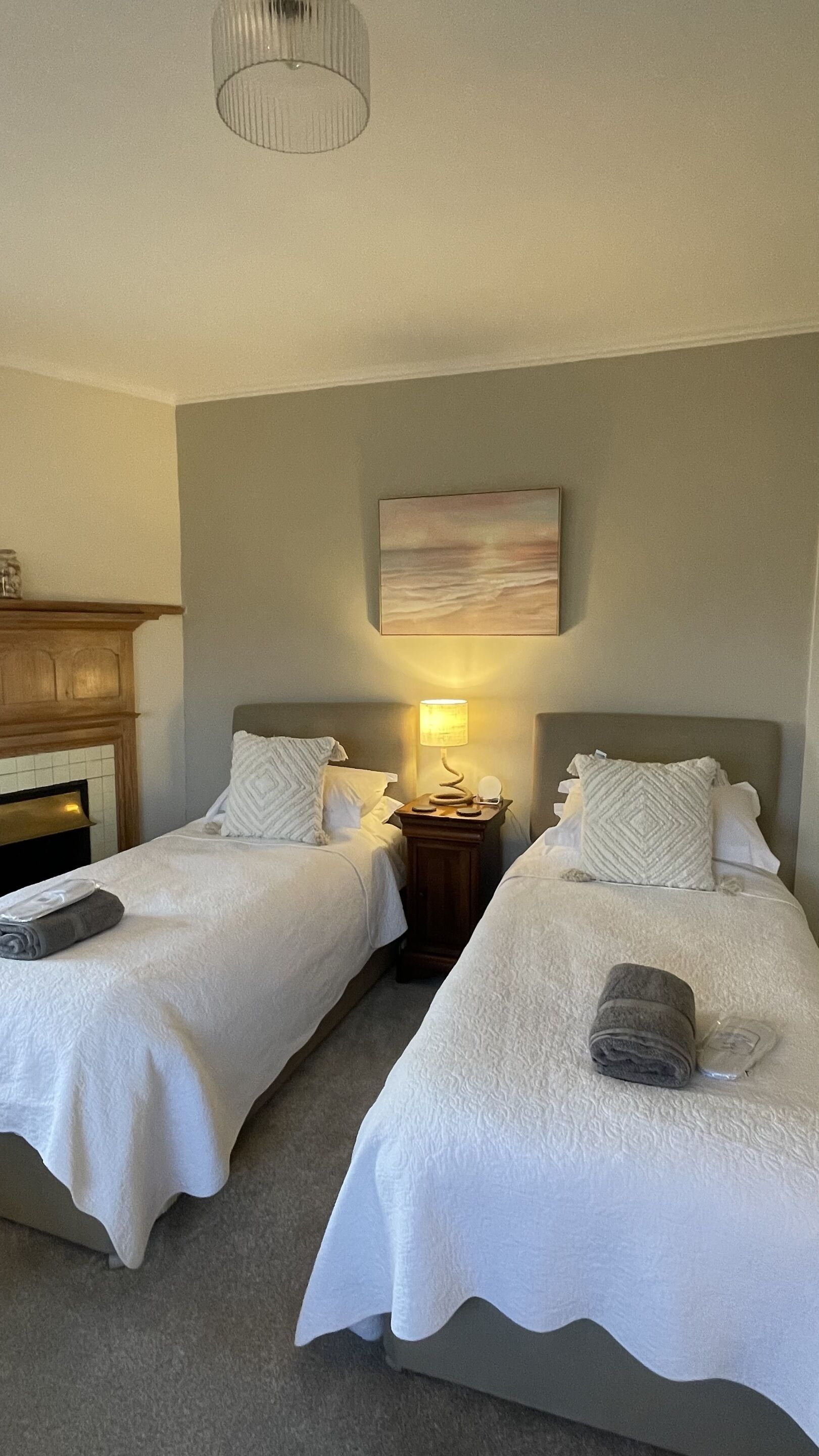 Habitación de hotel con dos camas, una mesita de noche con lámpara, un cuadro en la pared y un armario de madera.