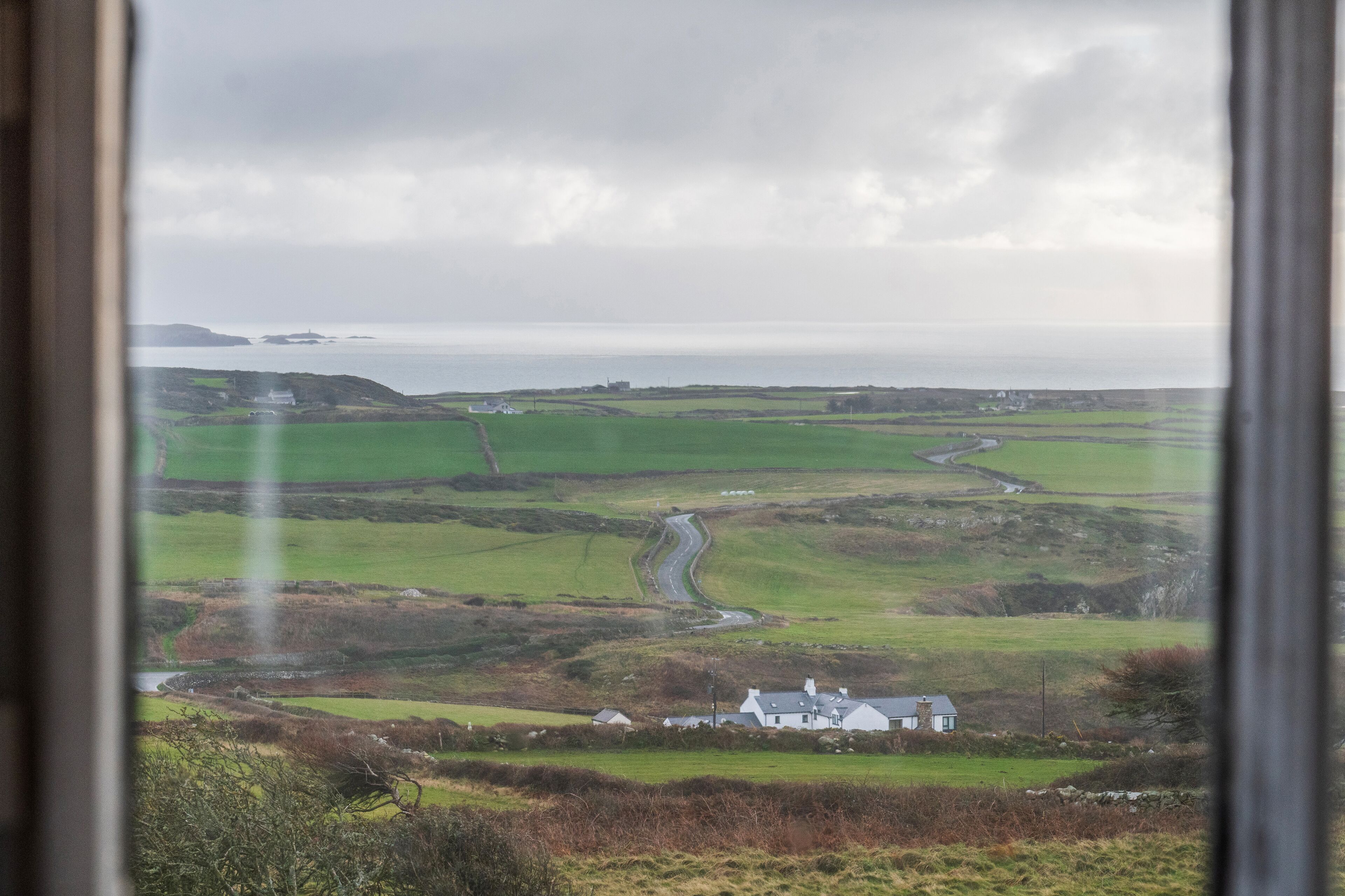 A rural landscape with a winding road, green fields, and a white house.