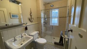 A bathroom with a glass-enclosed shower, a sink, a toilet, and a window.
