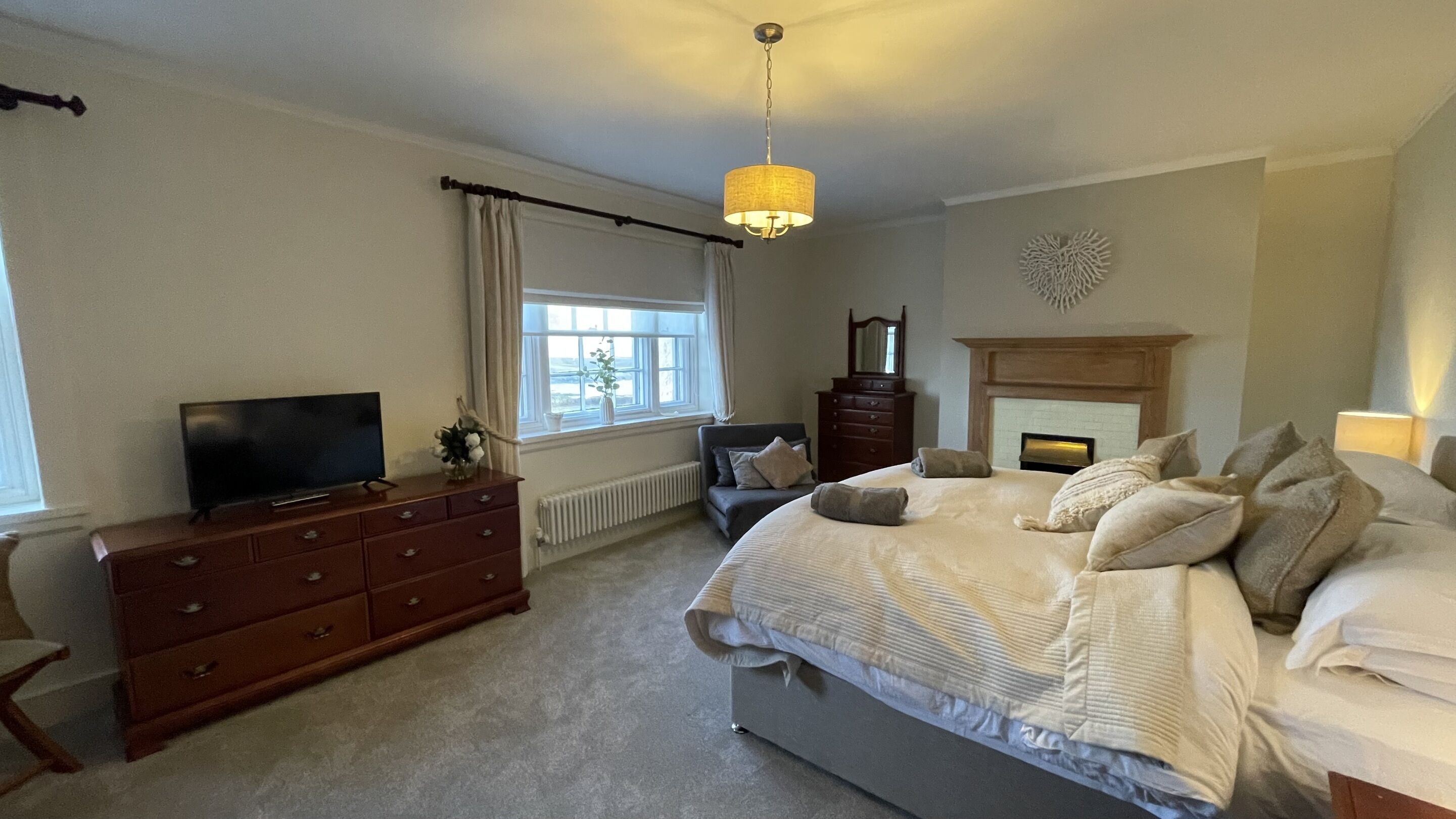 A bedroom with a bed, dresser, television, and a fireplace.