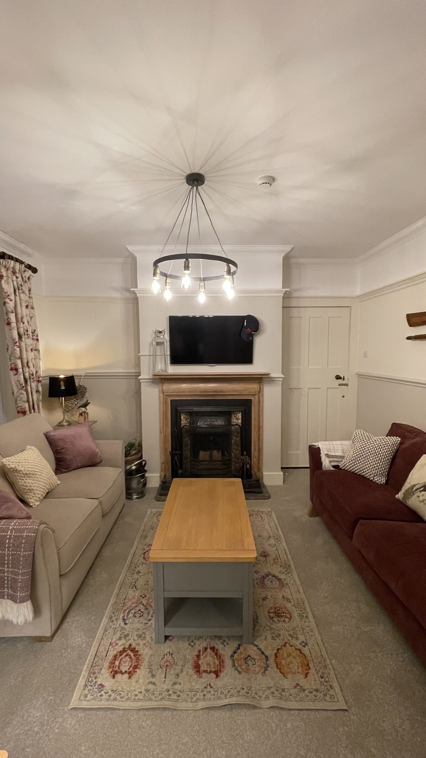 A living room with a fireplace, a television mounted above it, a sofa, a coffee table, and a patterned rug.