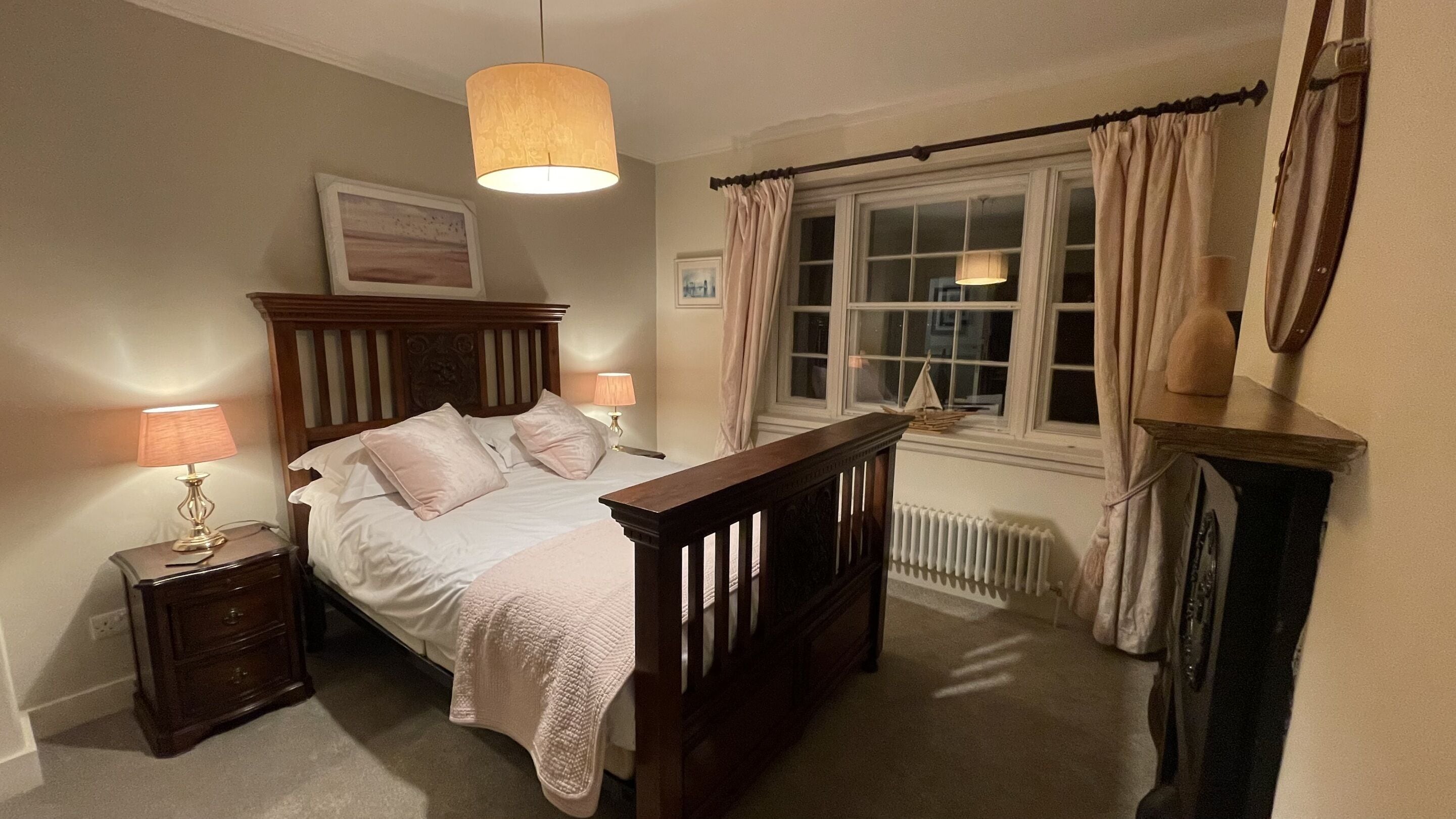 A bedroom with a wooden bed, bedside lamps, a window with curtains, and a radiator.