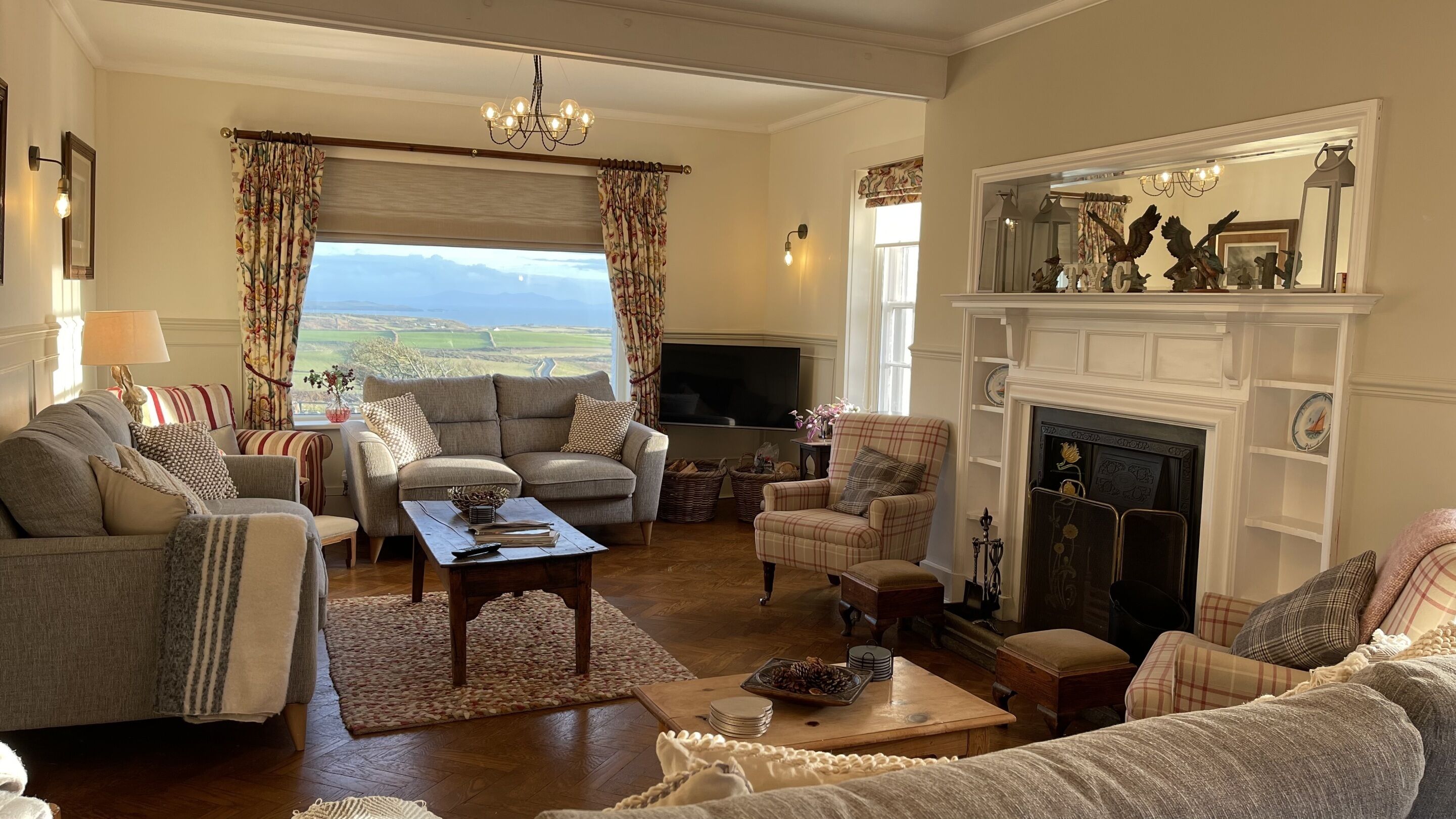 A cozy living room with a fireplace, comfortable seating, a television, and a view of the countryside.
