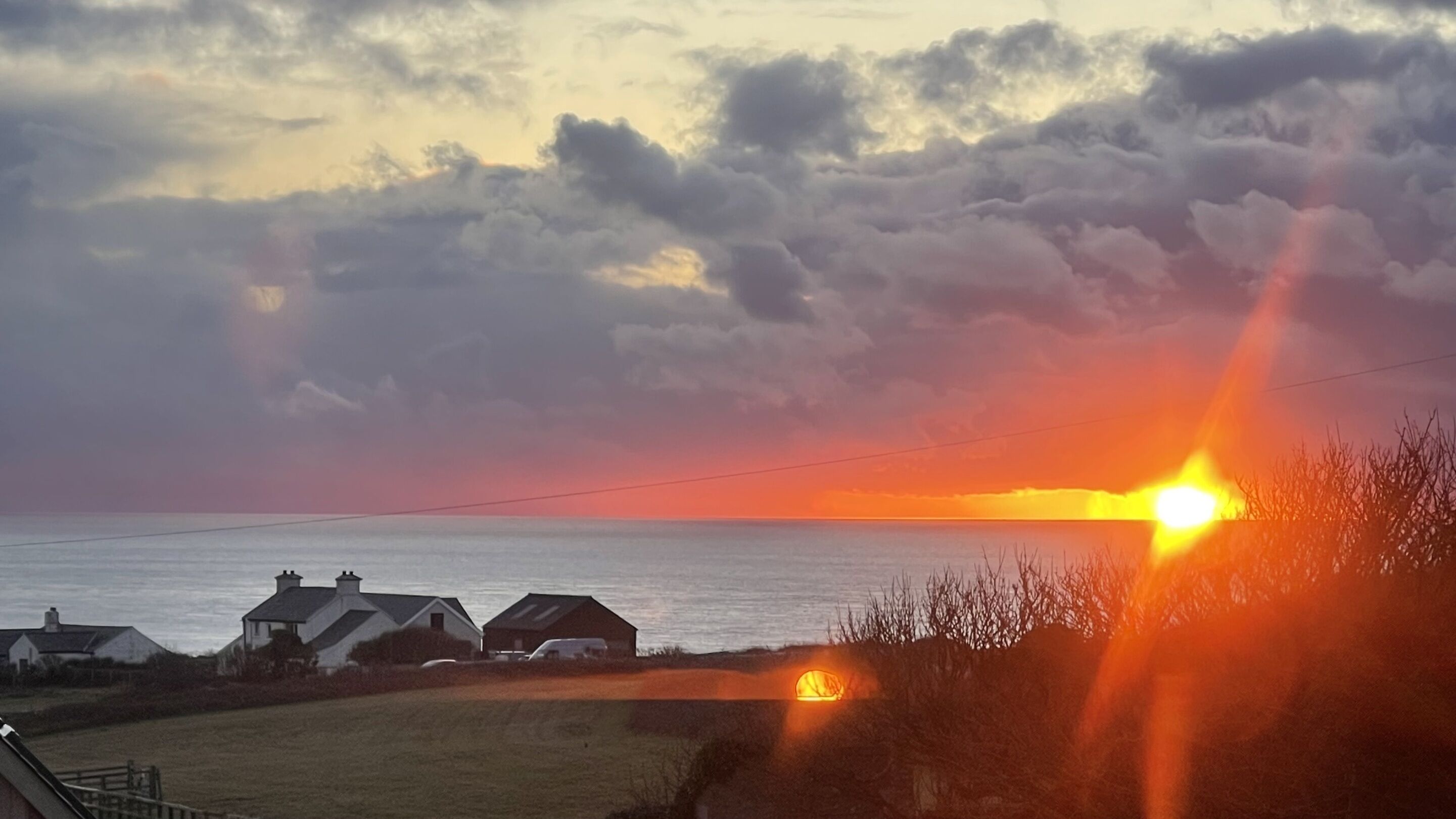 A sunset over a coastal area with houses and a clear sky.