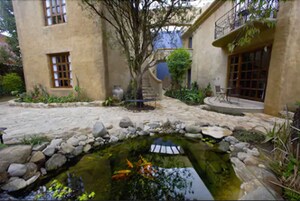 Un patio con un pequeño estanque, un sendero de piedra y un edificio con ventanas amplias y un balcón.