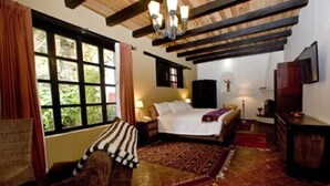 A cozy bedroom with a large bed, a wooden ceiling, a window with curtains, and a patterned rug.
