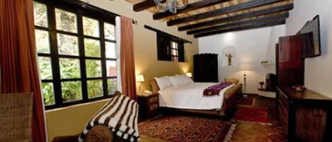 Un dormitorio acogedor con una cama grande, techo de madera, ventana con cortinas y una alfombra estampada.