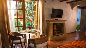 A cozy living room with a fireplace, a television mounted above it, and a dining area with two chairs and a table.