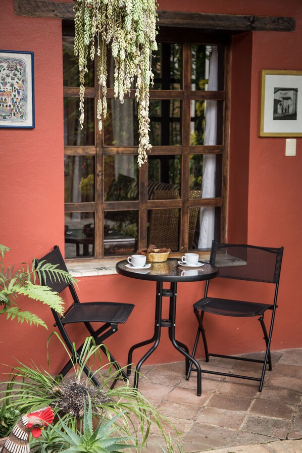 Um pátio acolhedor com mesa e cadeiras, planta pendente e quadros nas paredes.