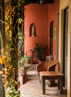 Un couloir étroit avec un banc en bois et une table, une plante en pot et une statue accrochée au mur.