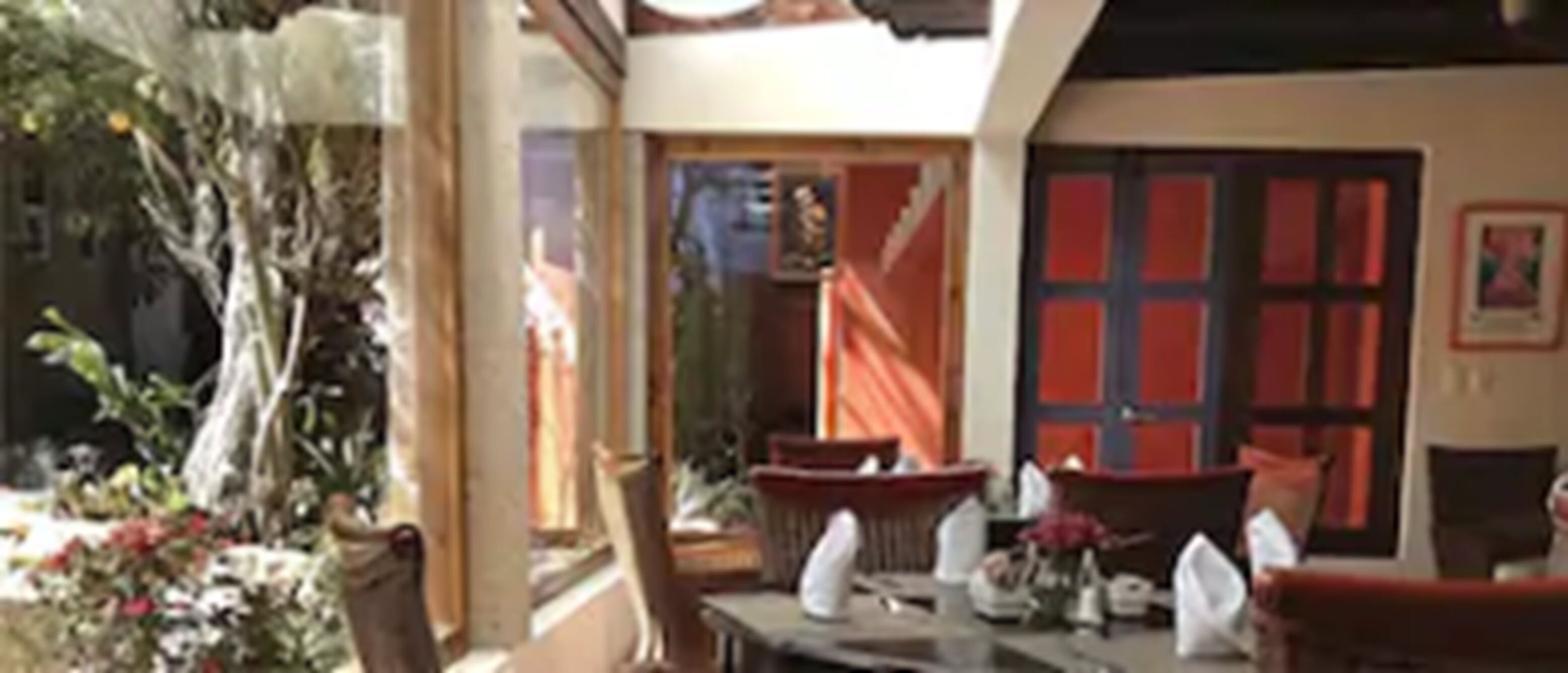 A room with a large window, a dining table with chairs, a red door, and a small plant.