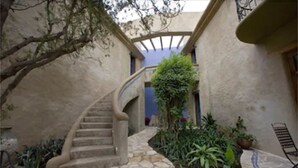 A stone staircase leading to a covered area with a blue wall, surrounded by potted plants and a small outdoor seating area.