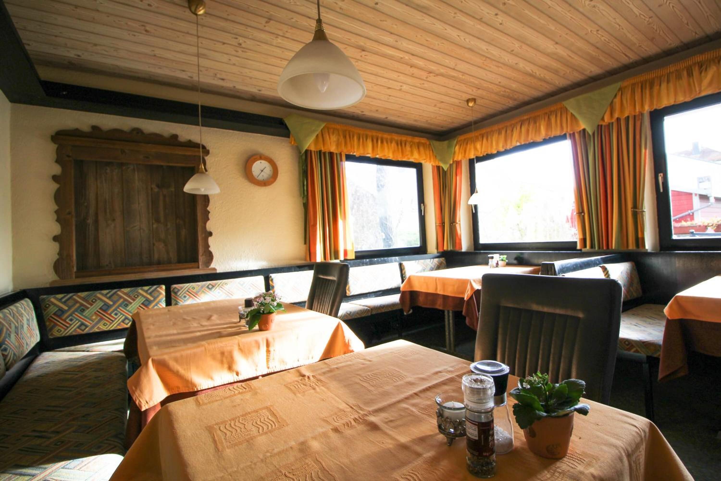 Interior de restaurante con techo de madera, manteles naranja y cortinas coloridas.