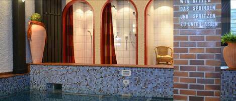 Ein modernes Badezimmer mit Mosaikboden, drei Rundduschen, einer Holzbank und einem Schild mit deutschem Text.