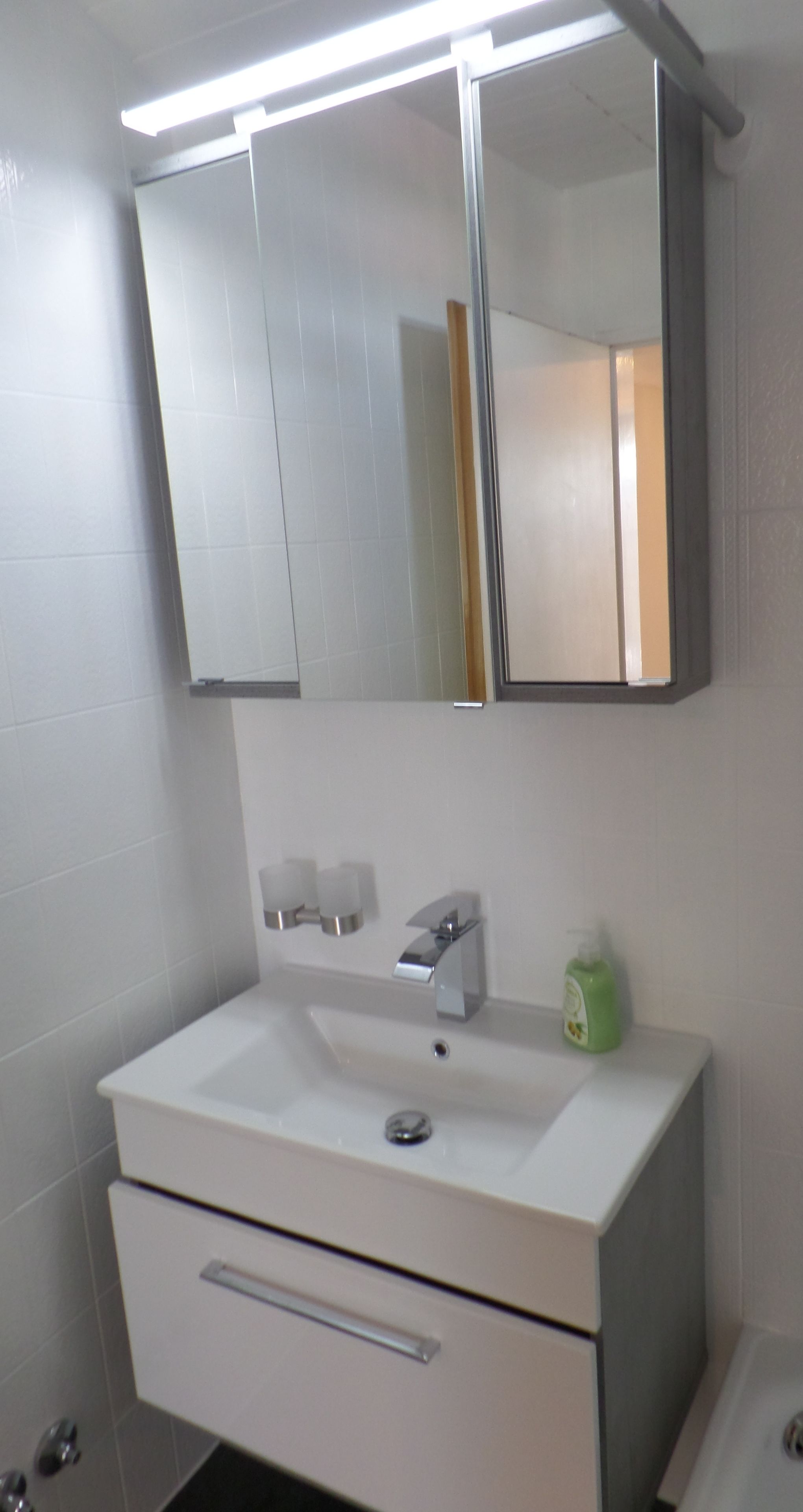 A bathroom with a white sink, a mirror, and a green bottle of hand soap.