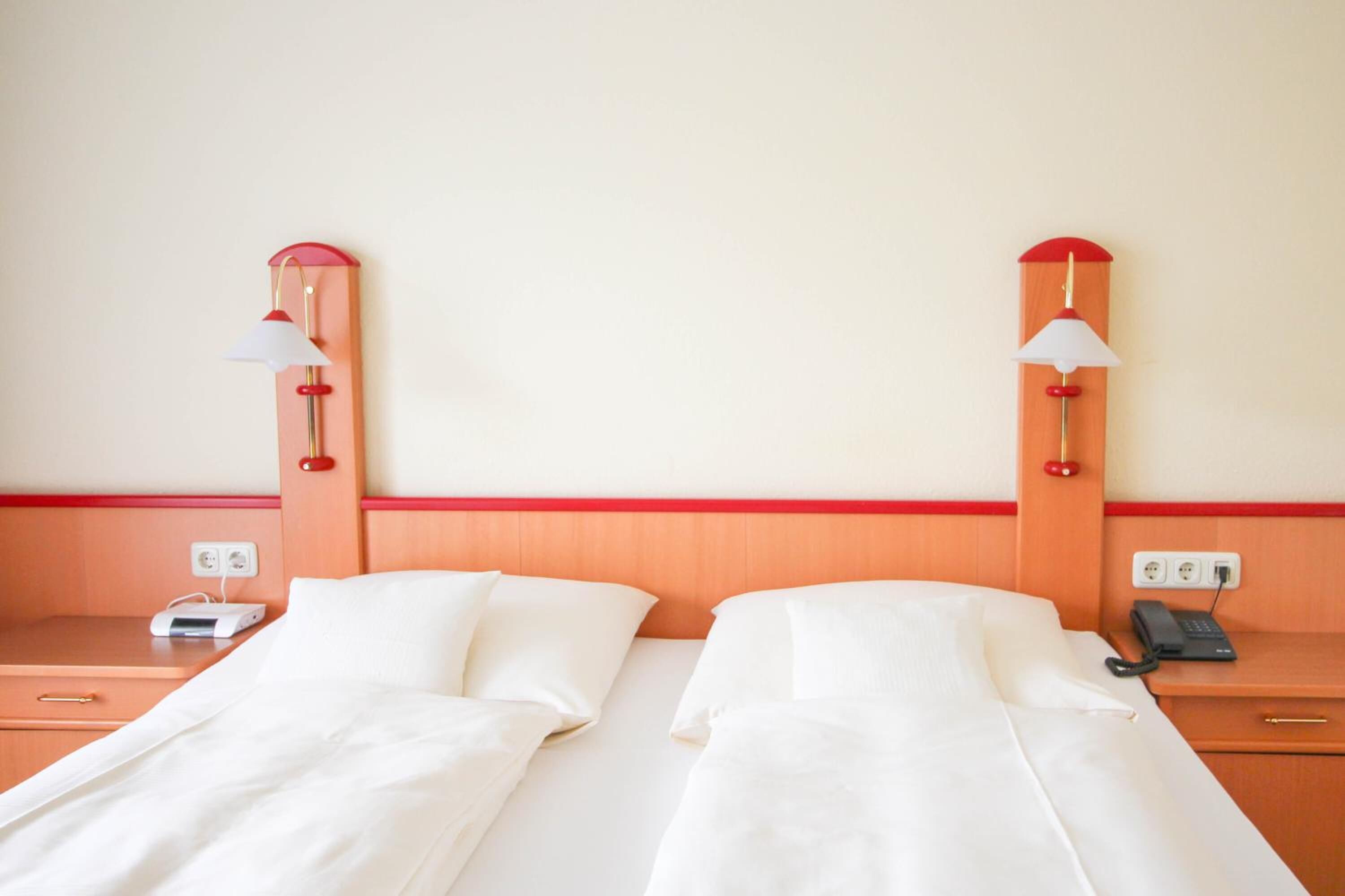 A hotel room with two beds, bedside tables, lamps, a phone, and a charging station.