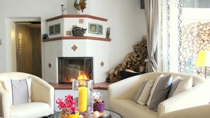 A living room with a fireplace, two sofas, a coffee table with flowers and candles, and a decorative shelf above the fireplace. - Hotel Brandl (Bad Woerishofen)