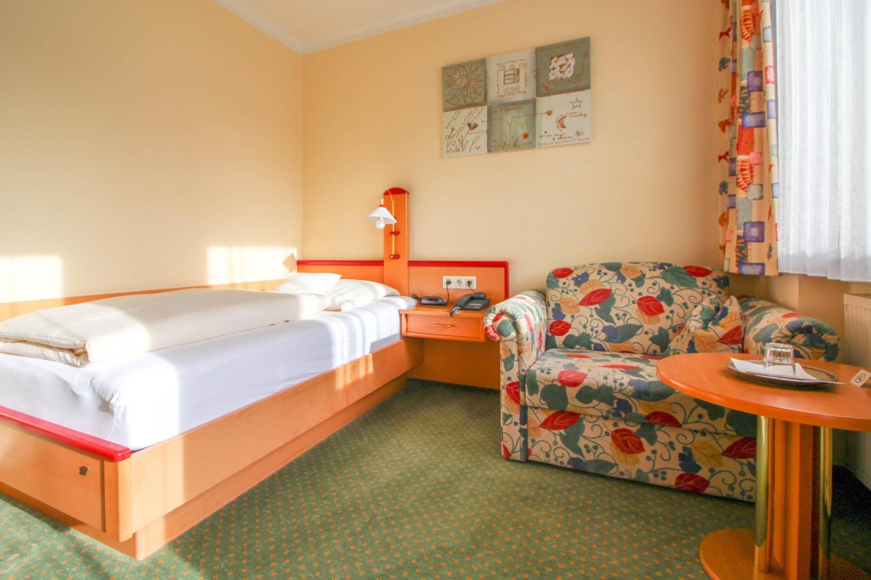 A hotel room with a bed, a chair, a small table, and a nightstand.