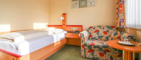 A hotel room with a bed, a chair, a small table, and a nightstand.