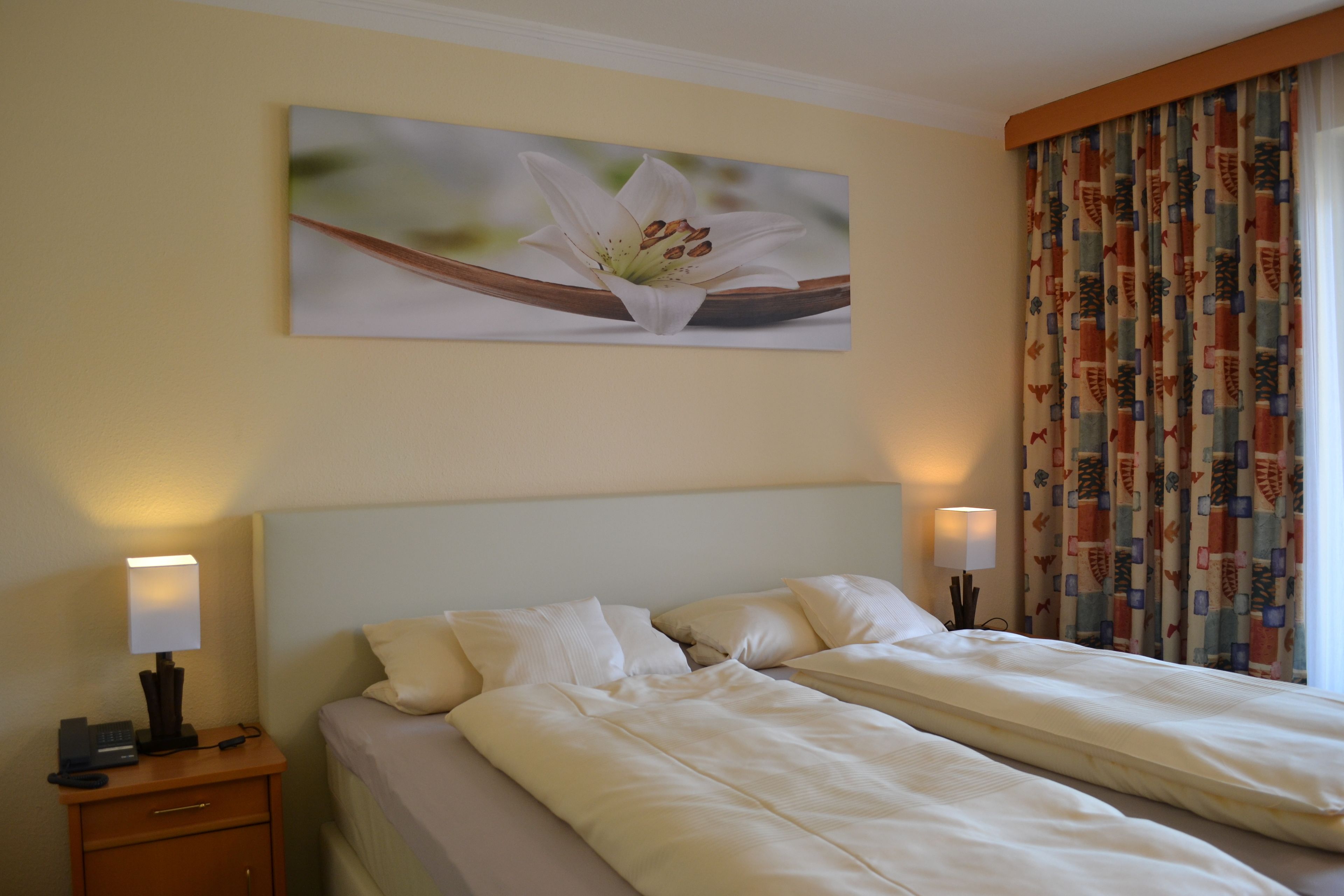 Une chambre d’hôtel avec un lit double, des lampes de chevet, une table de chevet et un tableau représentant une fleur accroché au mur.