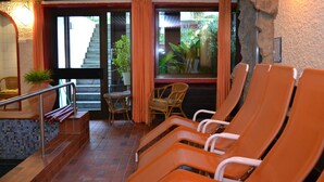 A spa area with orange chairs, a staircase, and a view of greenery outside. - Hotel Brandl (Bad Woerishofen)
