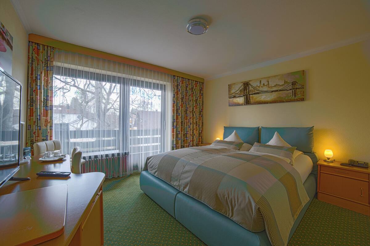 Habitación de hotel con una cama grande, un escritorio con computadora y teléfono, y una ventana con cortinas.