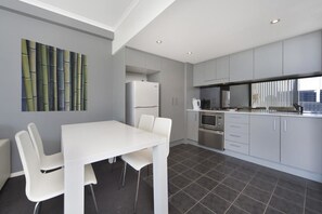A modern kitchen with white cabinetry, a white dining table with four chairs, and a large window providing natural light. - Astra Apartments - Paramatta (Parramatta)