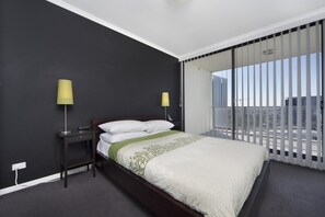 A modern hotel room with a large bed, two bedside lamps, a dark nightstand, and a view of the city through floor-to-ceiling windows. - Astra Apartments - Paramatta (Parramatta)