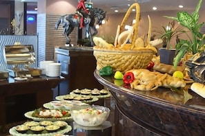 A buffet with various food items, a decorative horse statue, and potted plants. - Dongguan Hotel (Dongguan)