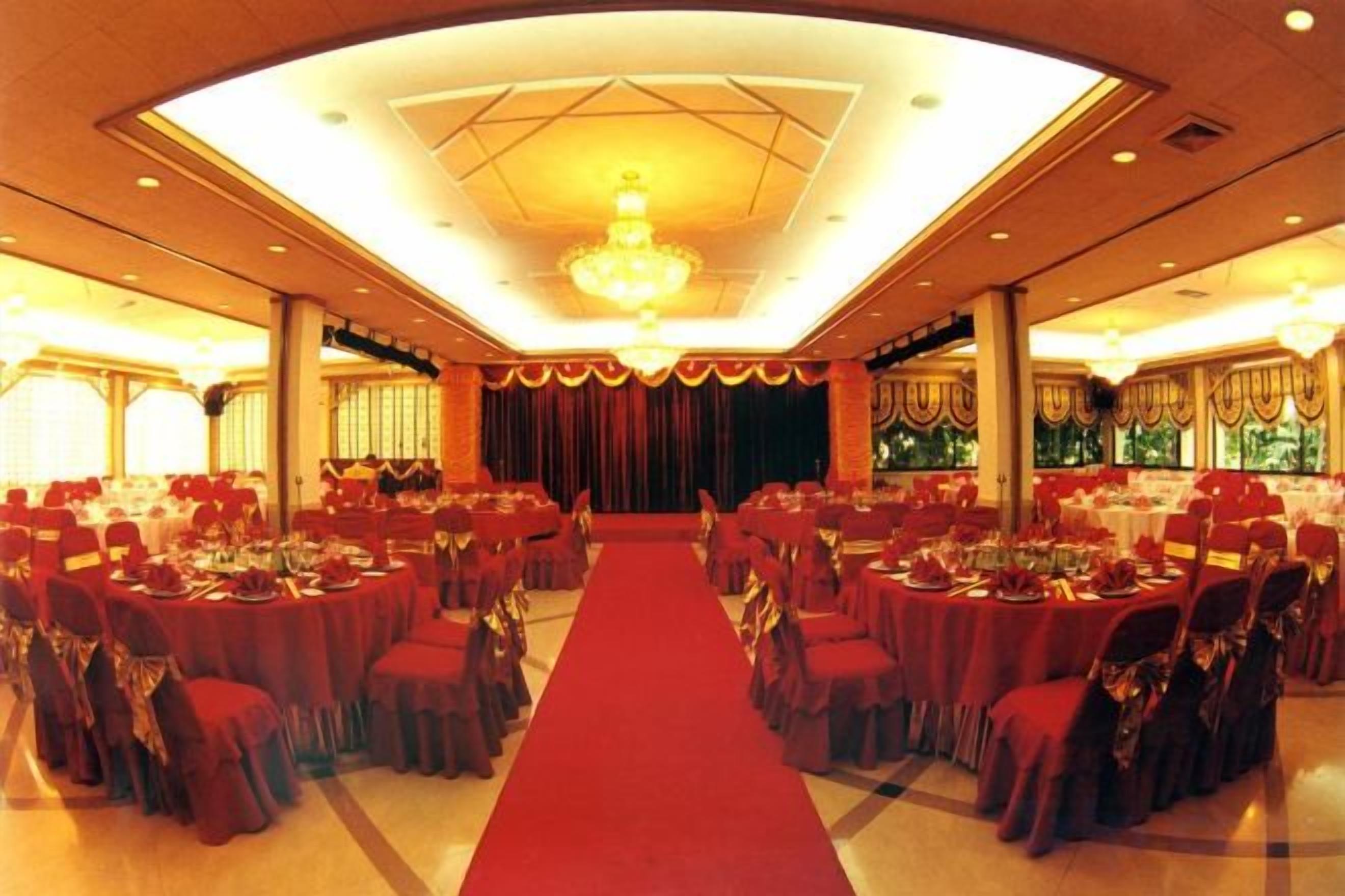 A banquet hall with round tables and chairs, a red carpet, and a chandelier.