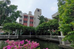 A building with a white facade and red accents, surrounded by greenery and a water feature. - Dongguan Hotel (Dongguan)