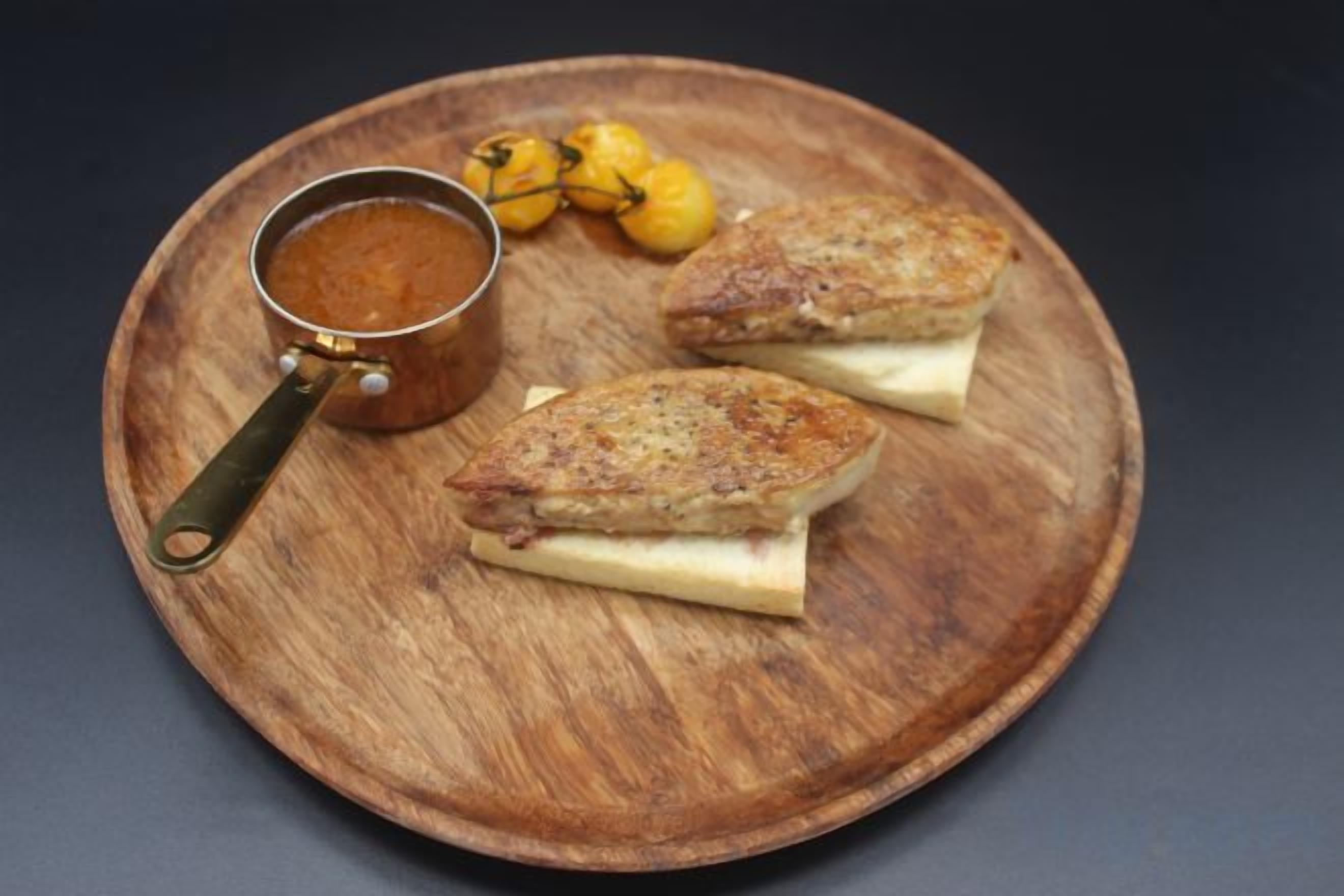 A wooden plate with two sandwiches and a small pot of sauce.