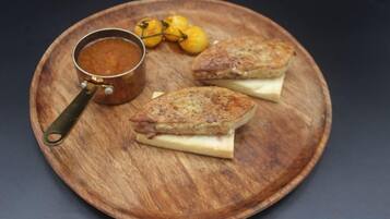 A wooden plate with two sandwiches and a small pot of sauce.