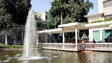A fountain in a park with a covered walkway and buildings in the background.