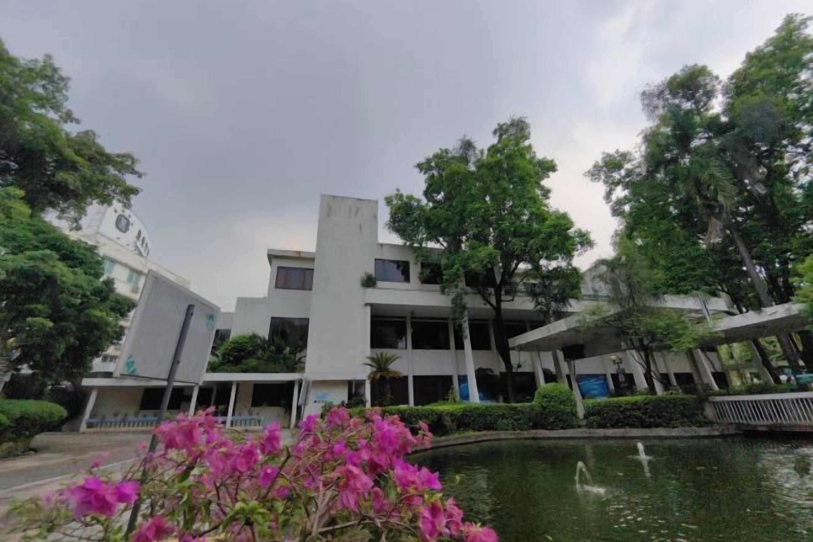 A modern building with a flat roof and a rectangular shape, surrounded by trees and a small pond.