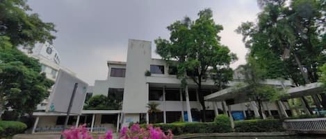 A modern building with a flat roof and a rectangular shape, surrounded by trees and a small pond.