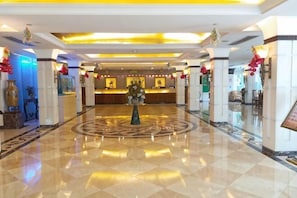 A hotel lobby with a reception desk, a circular decorative floor pattern, and a central column. - Dongguan Hotel (Dongguan)