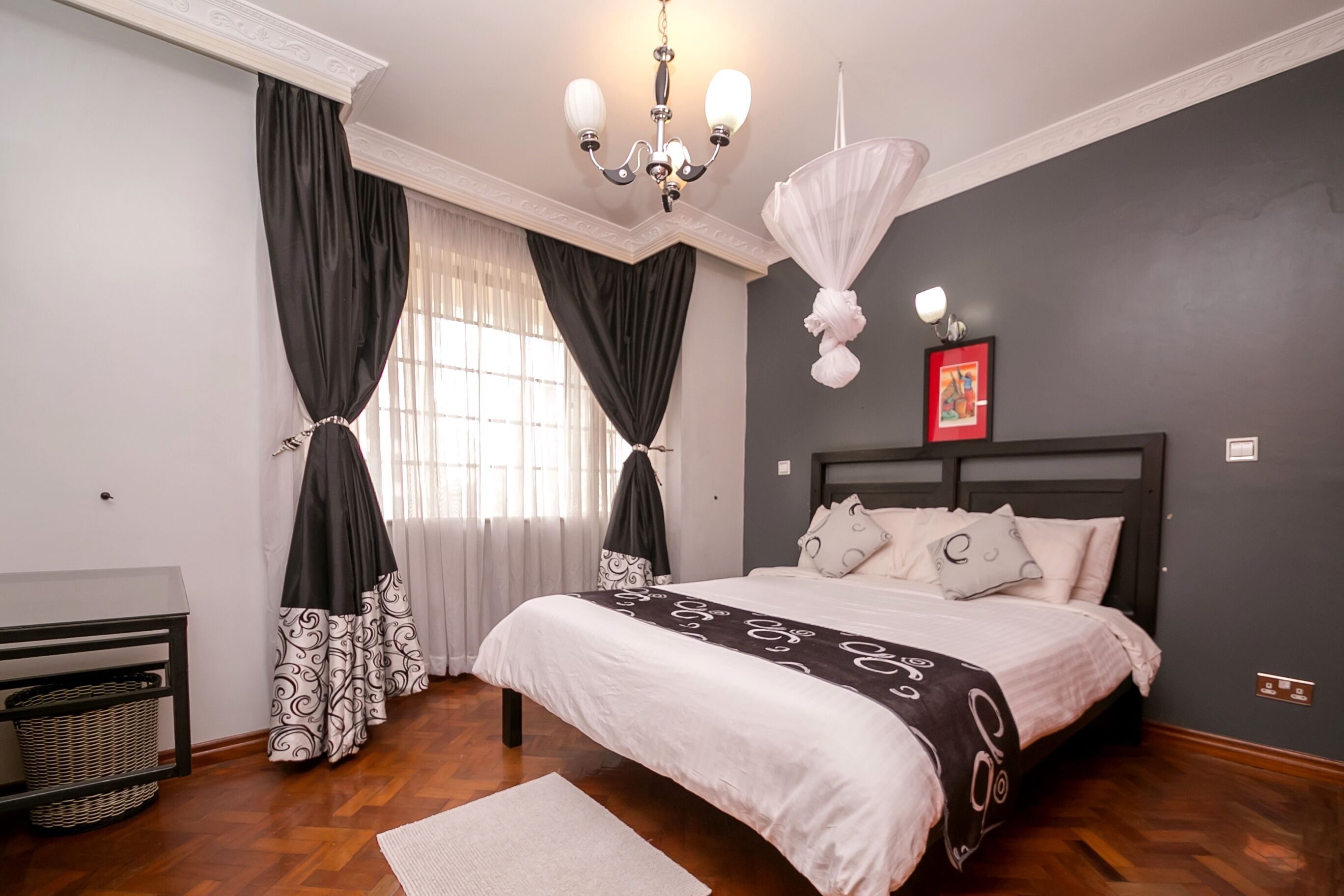 A bedroom with a bed, curtains, a chandelier, a picture frame, and a nightstand.