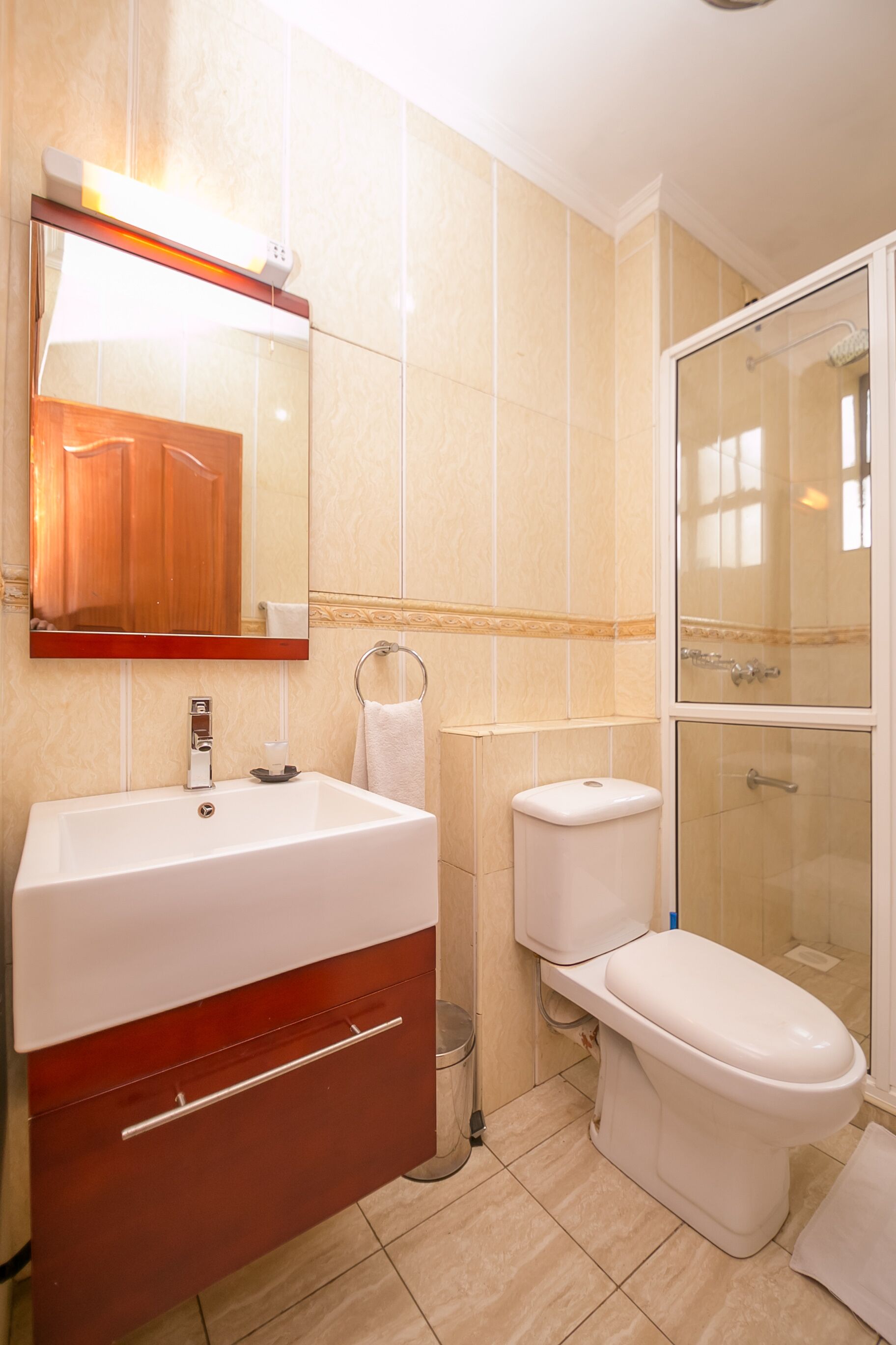 Une salle de bain avec un lavabo blanc, des toilettes, une douche en verre et un miroir au-dessus du lavabo.
