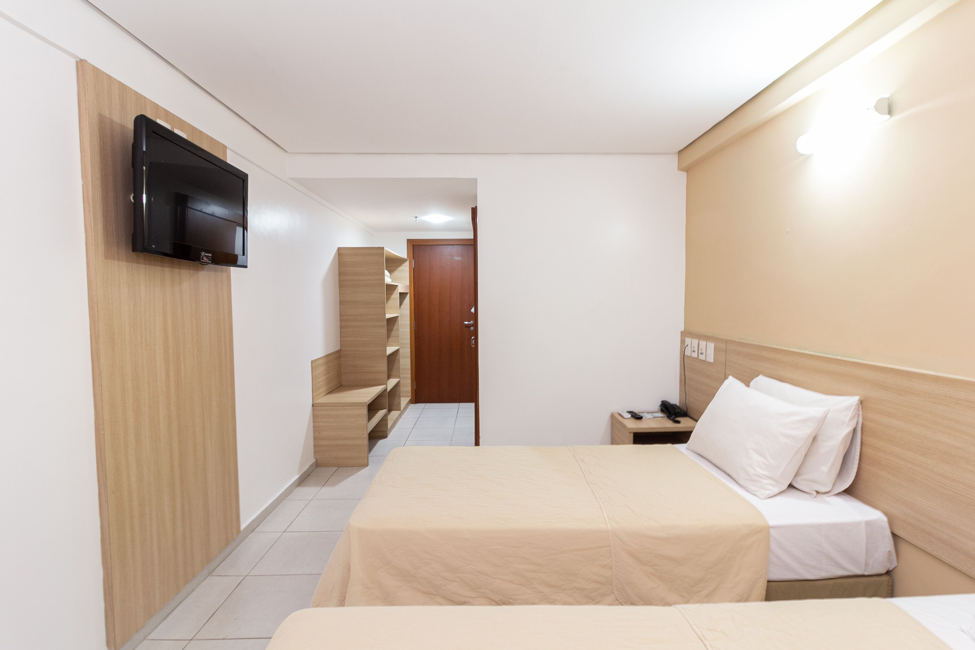 A hotel room with a bed, bedside table, and a TV mounted on the wall.