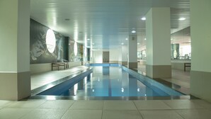 An indoor swimming pool with clear water, tiled walls, and a modern ceiling design.
