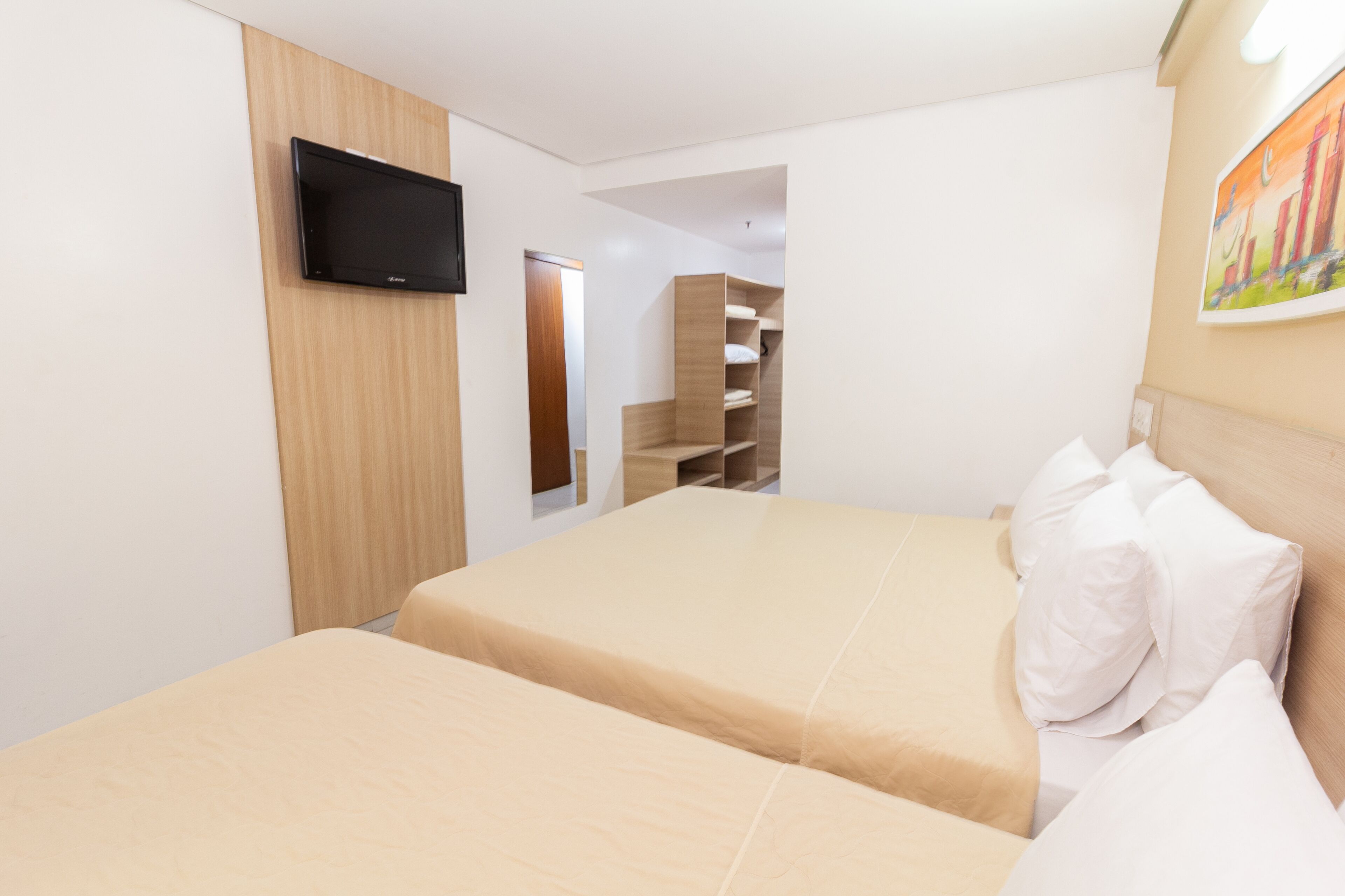 A hotel room with a bed, a TV mounted on the wall, and a painting on the wall.