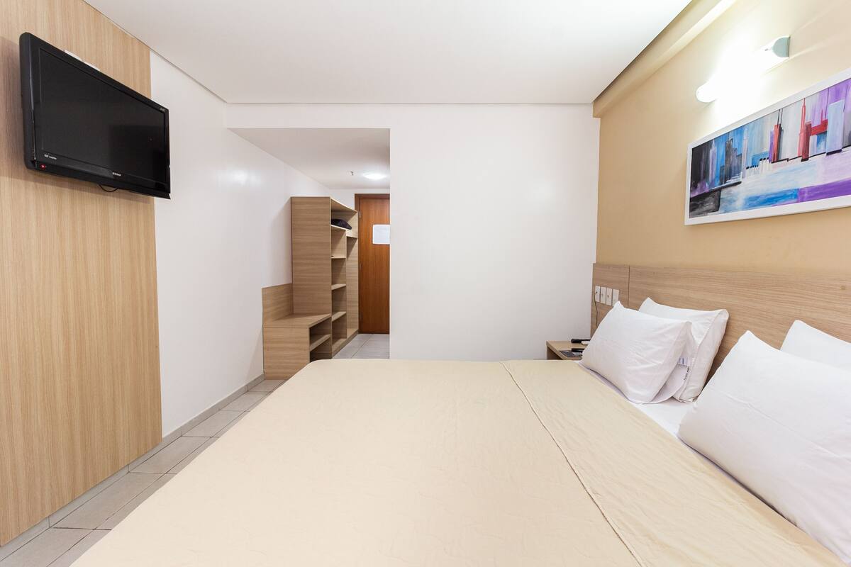 A modern hotel room with a large bed, a flat-screen TV mounted on the wall, and a painting above the bed.