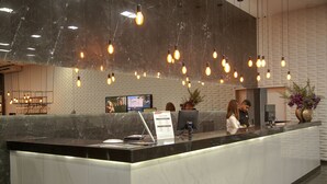 A hotel reception area with a marble counter, hanging light fixtures, a television screen, and a reception desk.