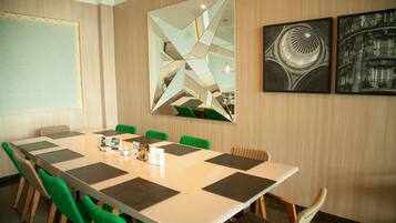 A conference room with a long table, green chairs, and a large mirror with geometric patterns.