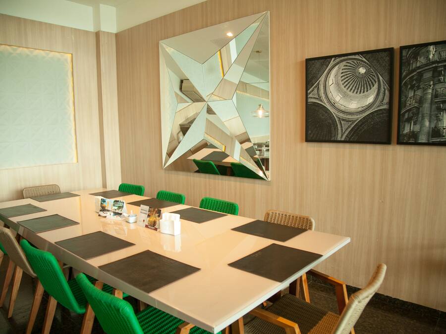 A conference room with a long table, green chairs, and a large mirror with geometric patterns.